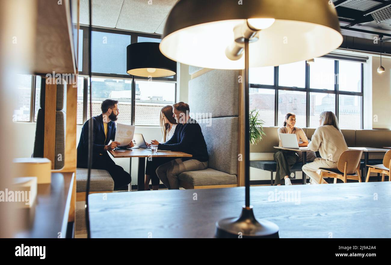 Geschäftsleute, die in einem modernen Co-Working-Raum arbeiten. Verschiedene Geschäftsleute, die Gespräche führen, während sie an einem offenen Arbeitsplatz sitzen. Entrepreneu Stockfoto