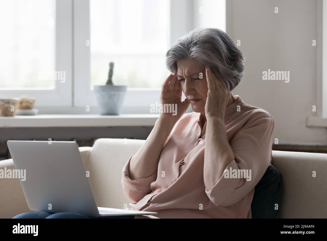 Gestresste ältere Frau, die den Kopf mit geschlossenen Augen berührt Stockfoto