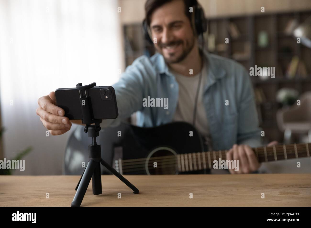 Männlicher Sänger mit Gitarre, der sein Smartphone auf den Halter setzt und die Übertragung startet Stockfoto