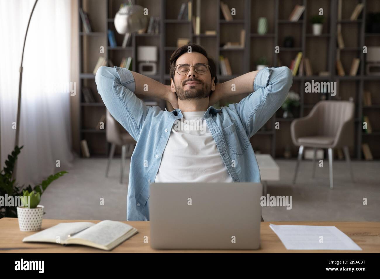 Glücklicher junger Mann, Freiberufler, entspannen sich am Schreibtisch und schließen die Augen Stockfoto