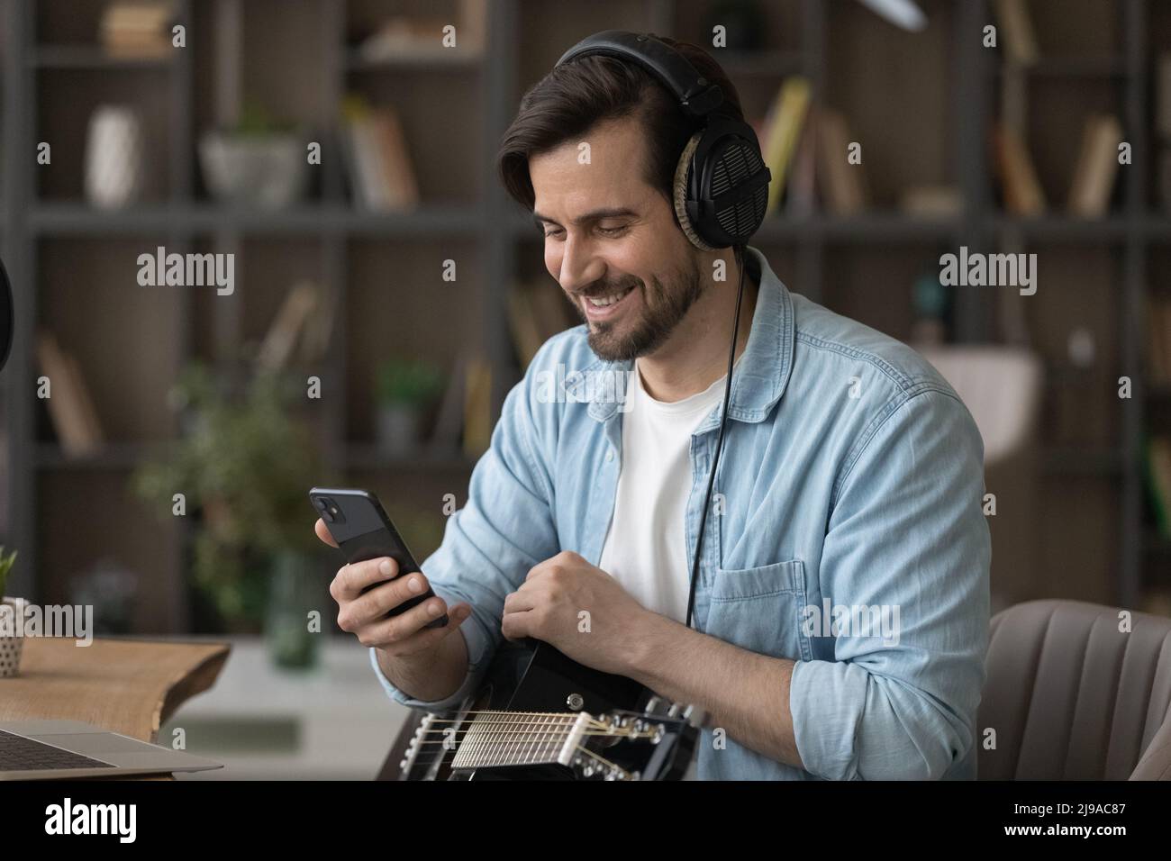 Millennial Mann Musiker im Headset halten Gitarre Telefonanruf machen Stockfoto