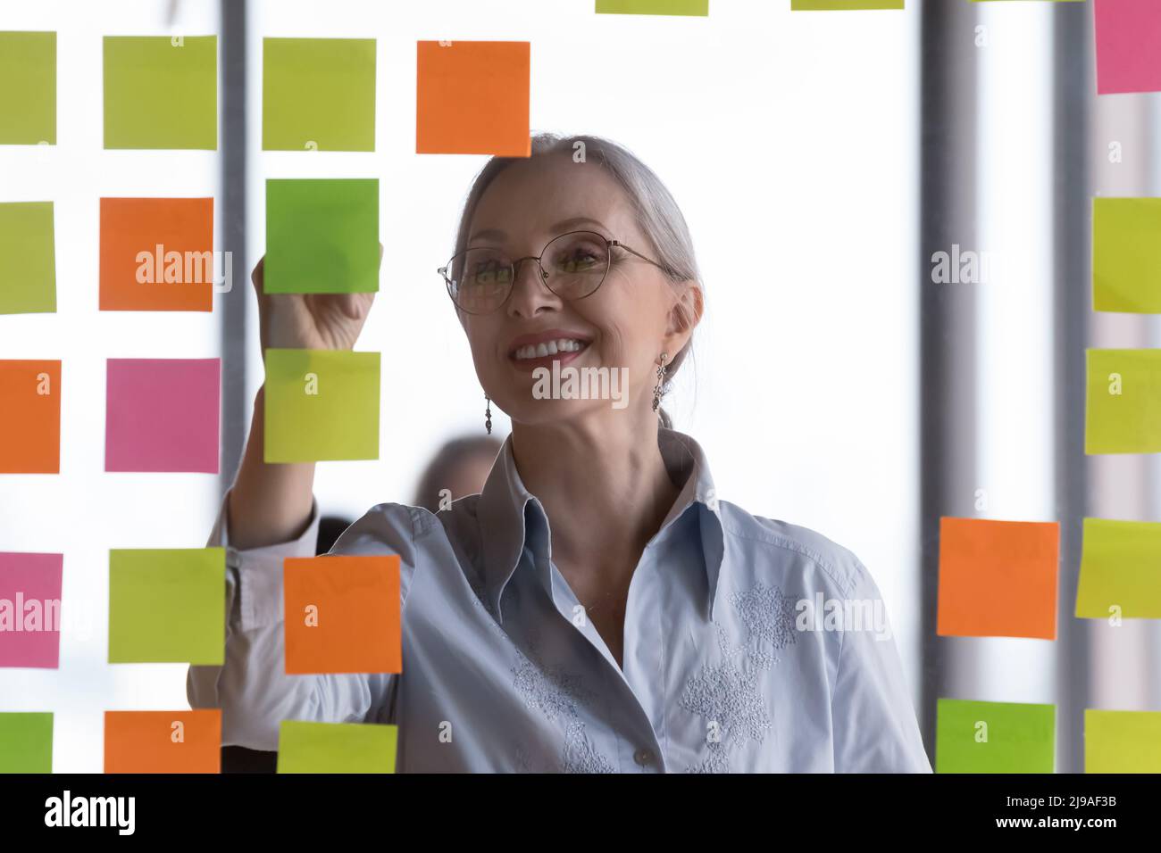 Eine lächelnde Geschäftsfrau mittleren Alters schreibt auf angehängten Haftnotizen Stockfoto