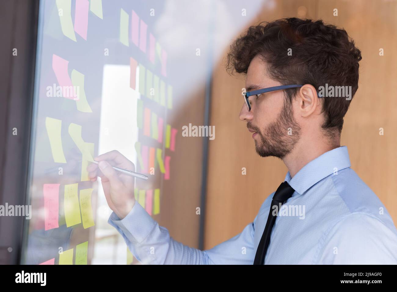 Der Geschäftsmann schreibt Informationen auf Haftnotizen, die an die Wand angebracht sind Stockfoto