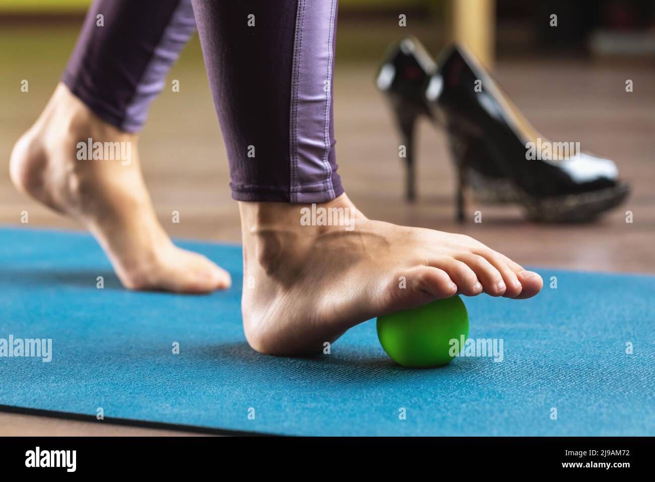 Eine Frau führt mit einem Massageball entspannende Übungen der Fußmuskeln durch, um nach dem Tragen von Schuhen mit hohen Absätzen Beinmüdigkeit zu verhindern Stockfoto