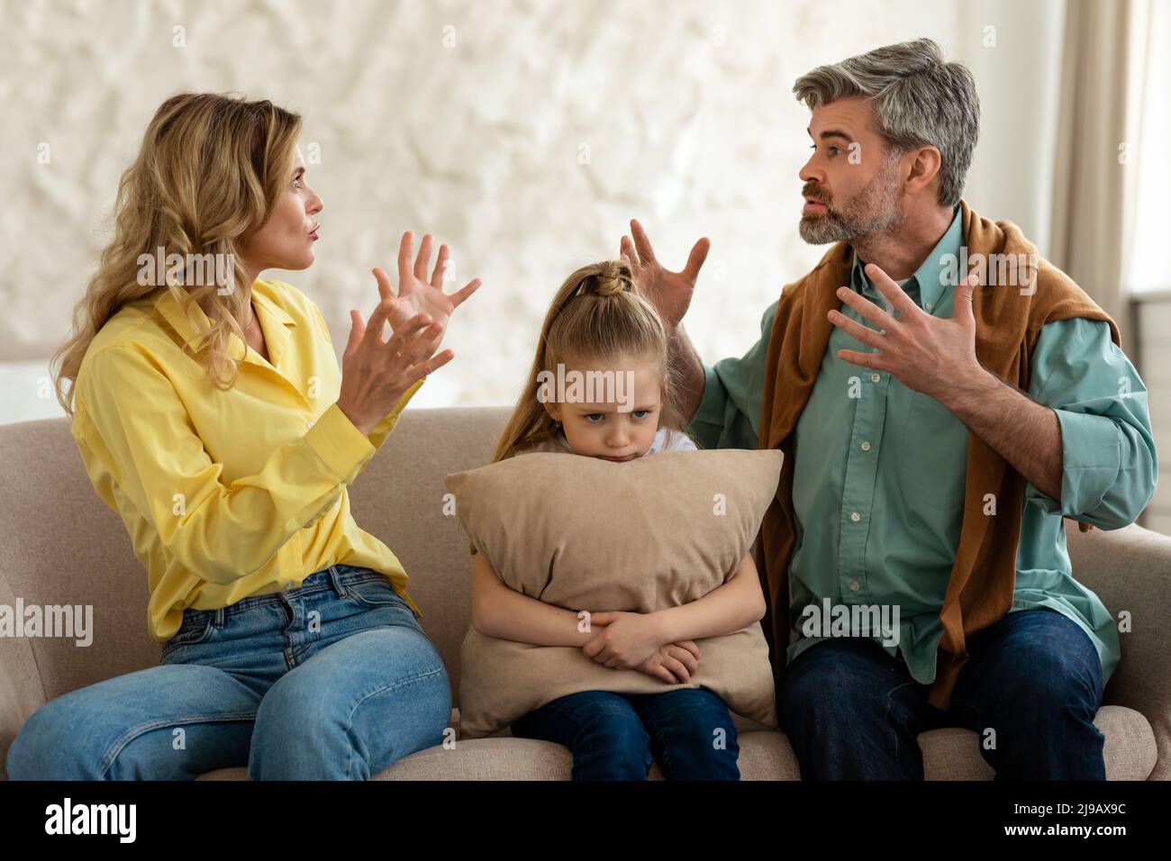 Unglückliche Tochter, Die Zwischen Den Eltern Sitzt, Während Sie Sich Im Freien Streiten Stockfoto