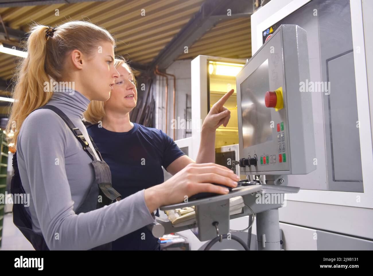 Eine weibliche Auszubildende erhält von ihrer Ausbilderin technischen Unterricht. Beide Frauen arbeiten als computergesteuerte numerische Steuerungstechniker. Stockfoto