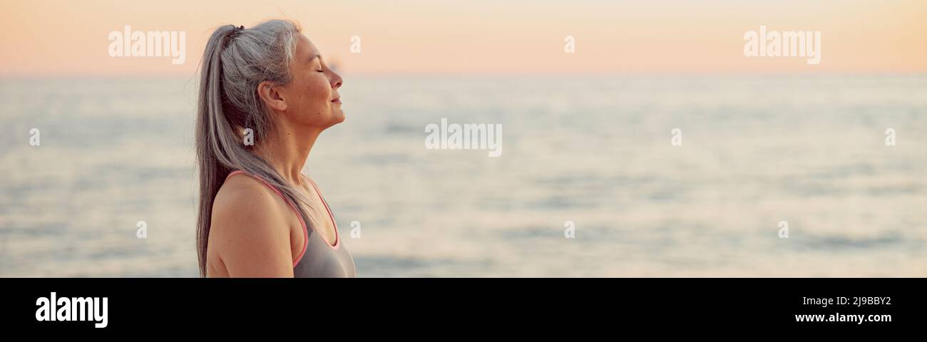 Reife Frau, die am Meer sitzt und den Sonnenuntergang genießt Stockfoto