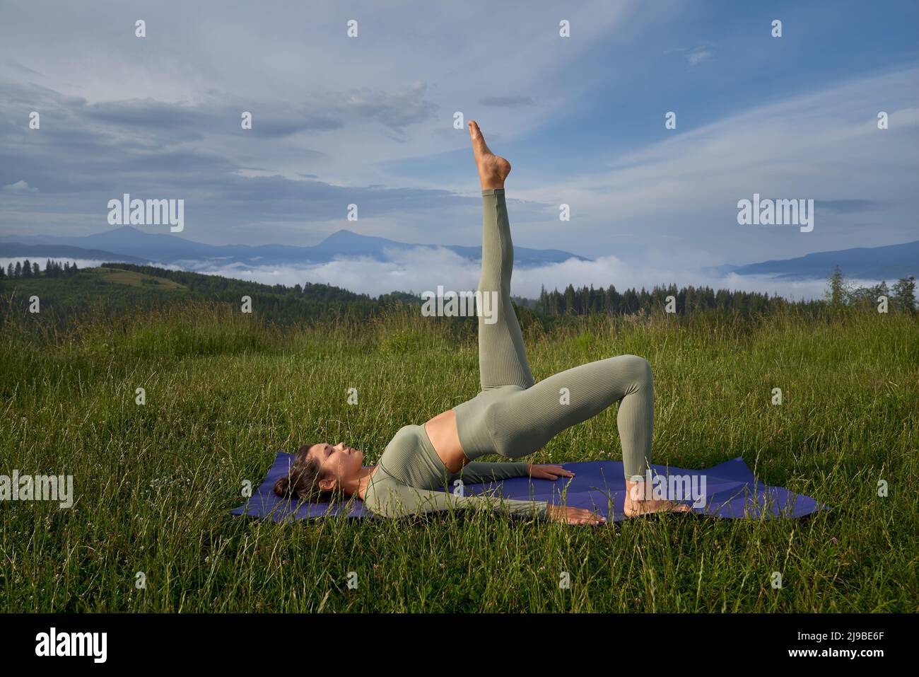 Sportliche junge Frau in Sportkleidung, die im Sommer unter den Bergen Yoga praktiziert. Konzept der Flexibilität, Balance und Konzentration. Stockfoto