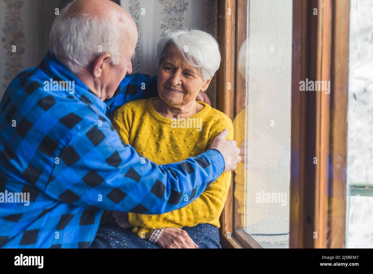 Seniorenpaar umarmt sich vor dem Fenster Medium shot Indoor Senior People Support Concept. Hochwertige Fotos Stockfoto