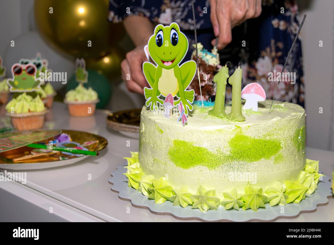 Schneiden Sie die Frosch-Motto elften Geburtstag Party Kuchen. Kindergeburtstag, glückliche Familienveranstaltungen. Home Events. Elf Jahre alte Kerzen auf einem Geburtstagskuchen. Stockfoto