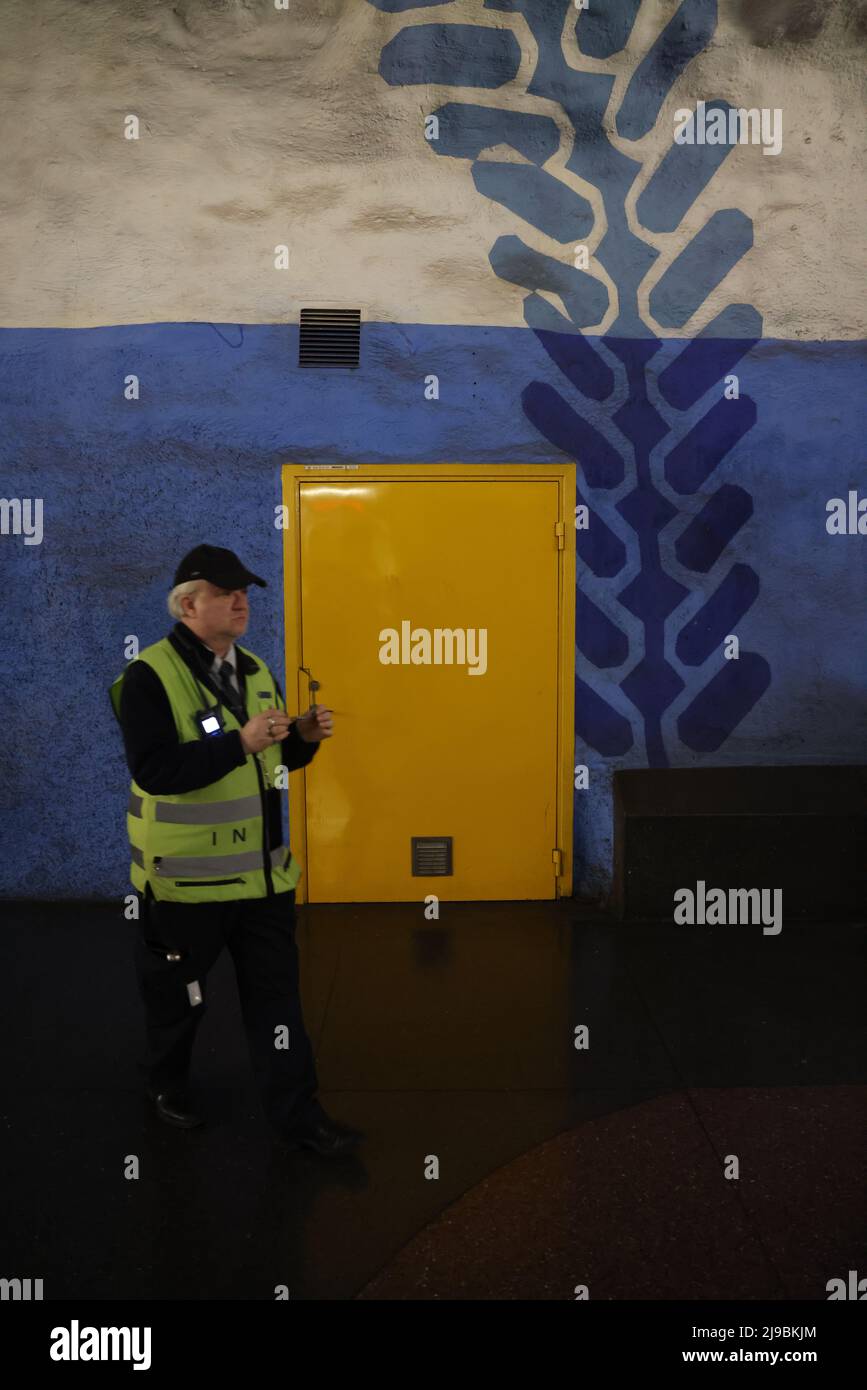 Gelbe Tür in blauer (und weißer) Felswand in der U-Bahnstation T-Centralen (Hauptbahnhof) in Stockholm; ein Mann in gelber Weste kommt vorbei Stockfoto