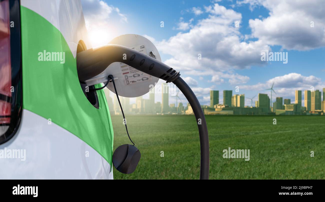 Nahaufnahme eines Elektroautos mit angeschlossenem Ladekabel auf dem Hintergrund der grünen Öko-Stadt Stockfoto