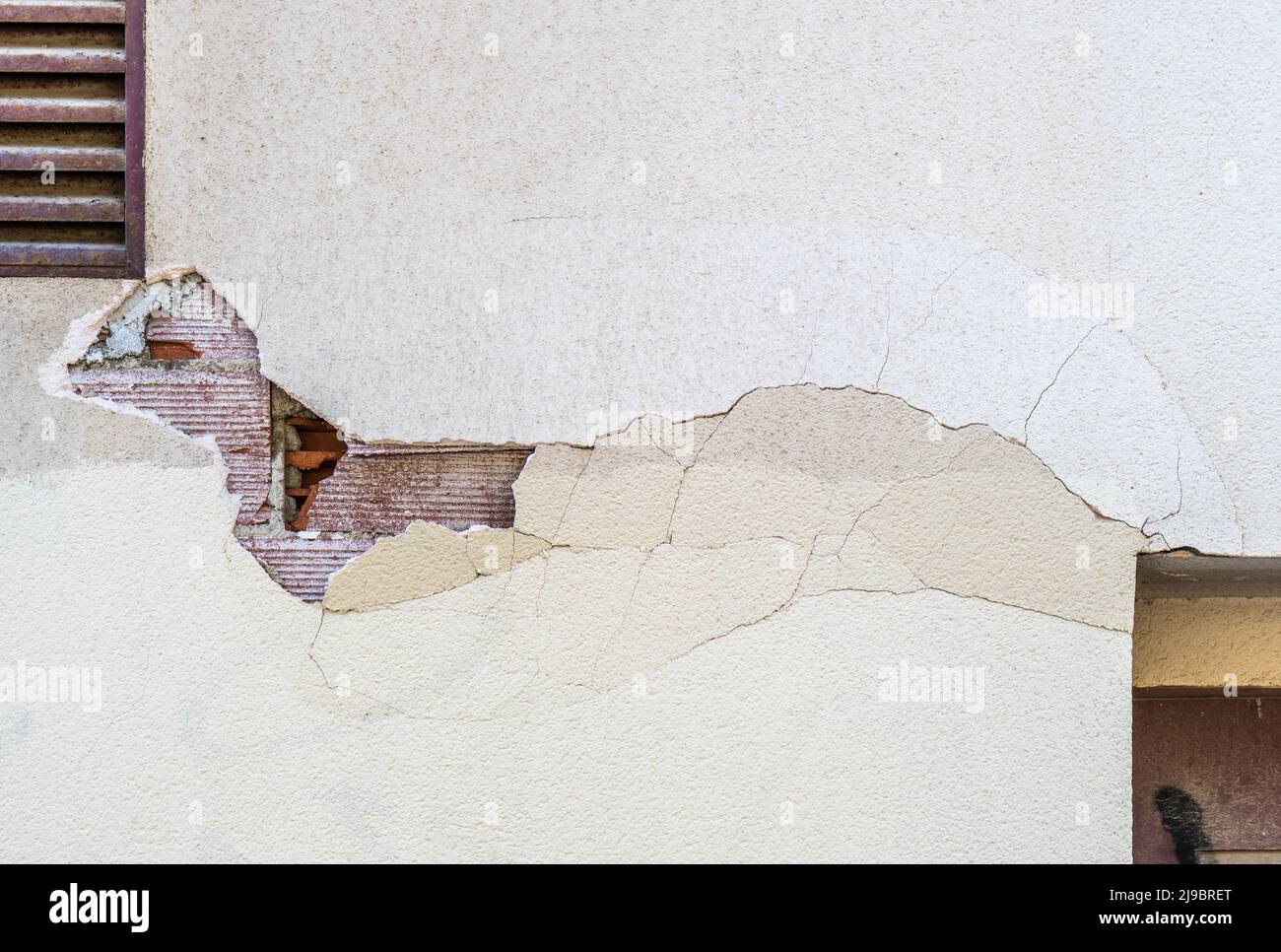 Beschädigte Gebäudefassade fällt, sichtbare Ziegel an der Wand befinden sich hinter zerbrochenen, zerklüfteten Betonoberflächen Stockfoto