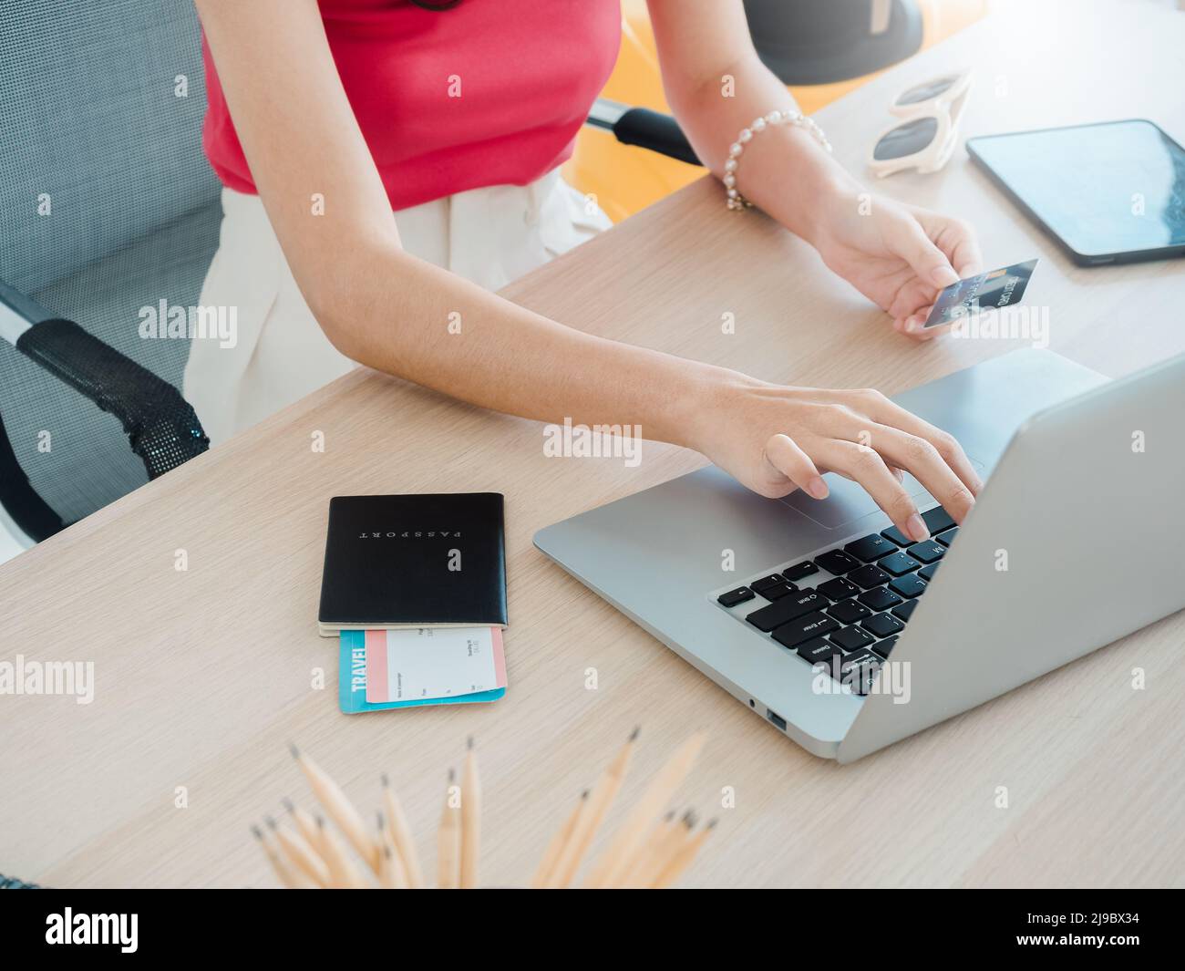 Die Hand der jungen Frau hält Kreditkarte und Reisepass, während sie den Laptop für die Flugbuchung benutzt, das Hotelzimmer für die Sommerreise auf dem Tisch, bereit für die Reise Stockfoto