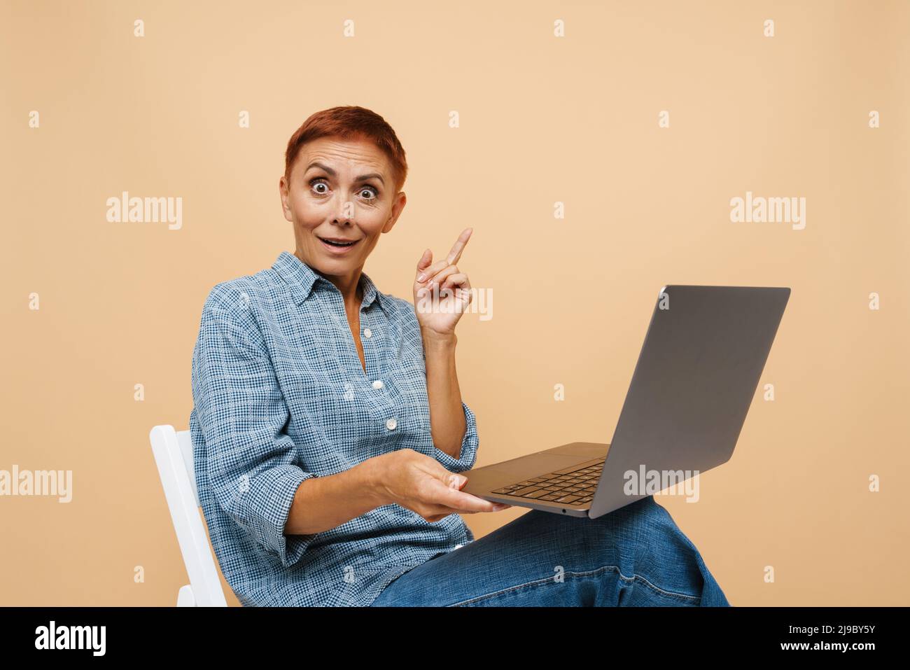 Senior überraschte Frau beim Arbeiten mit einem Laptop, der über einer beigen Wand isoliert war Stockfoto