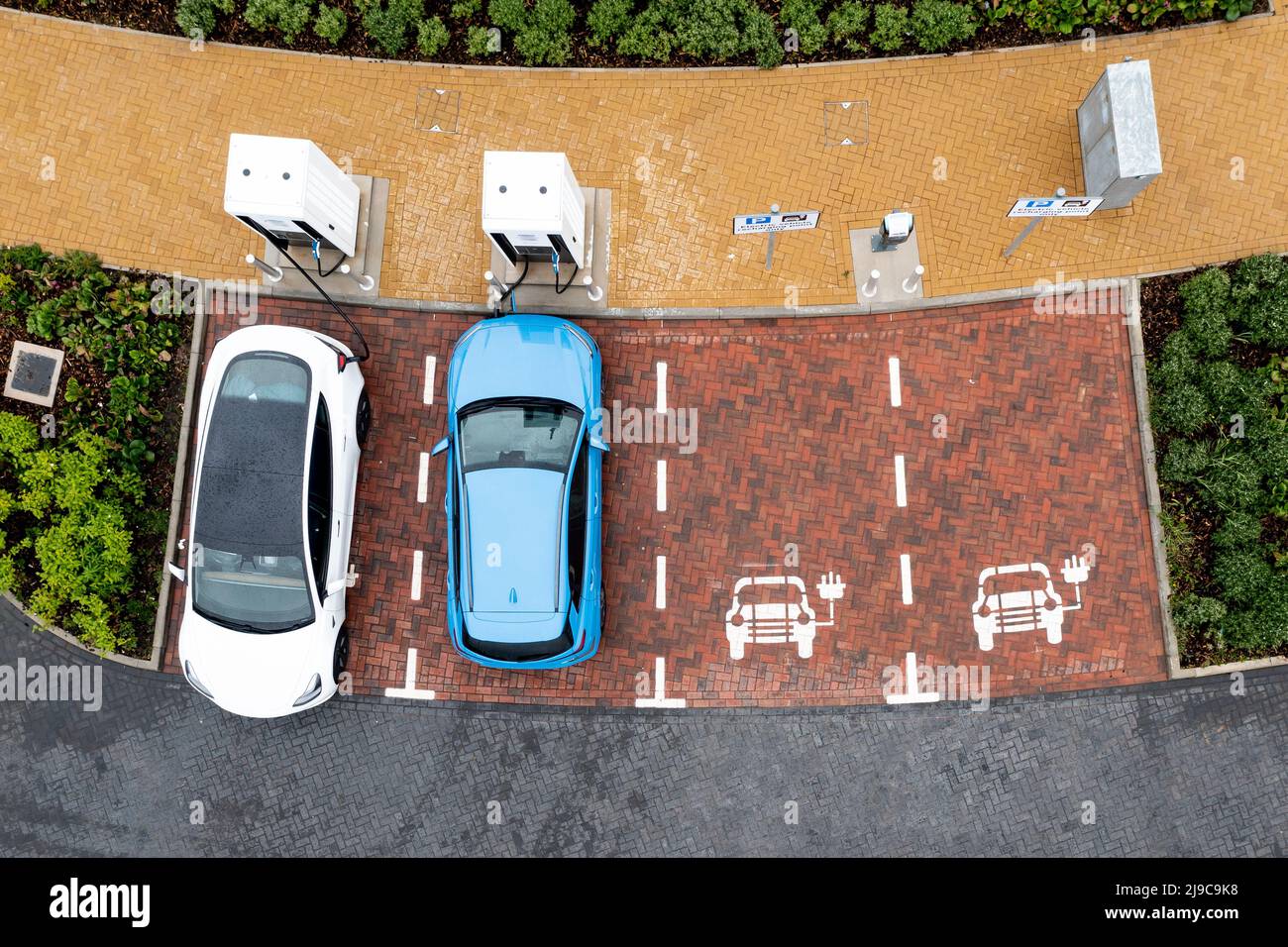 Eine Luftaufnahme direkt über Elektroautos, die an einer Autoladestation der Autobahn-Tankstelle geladen werden Stockfoto