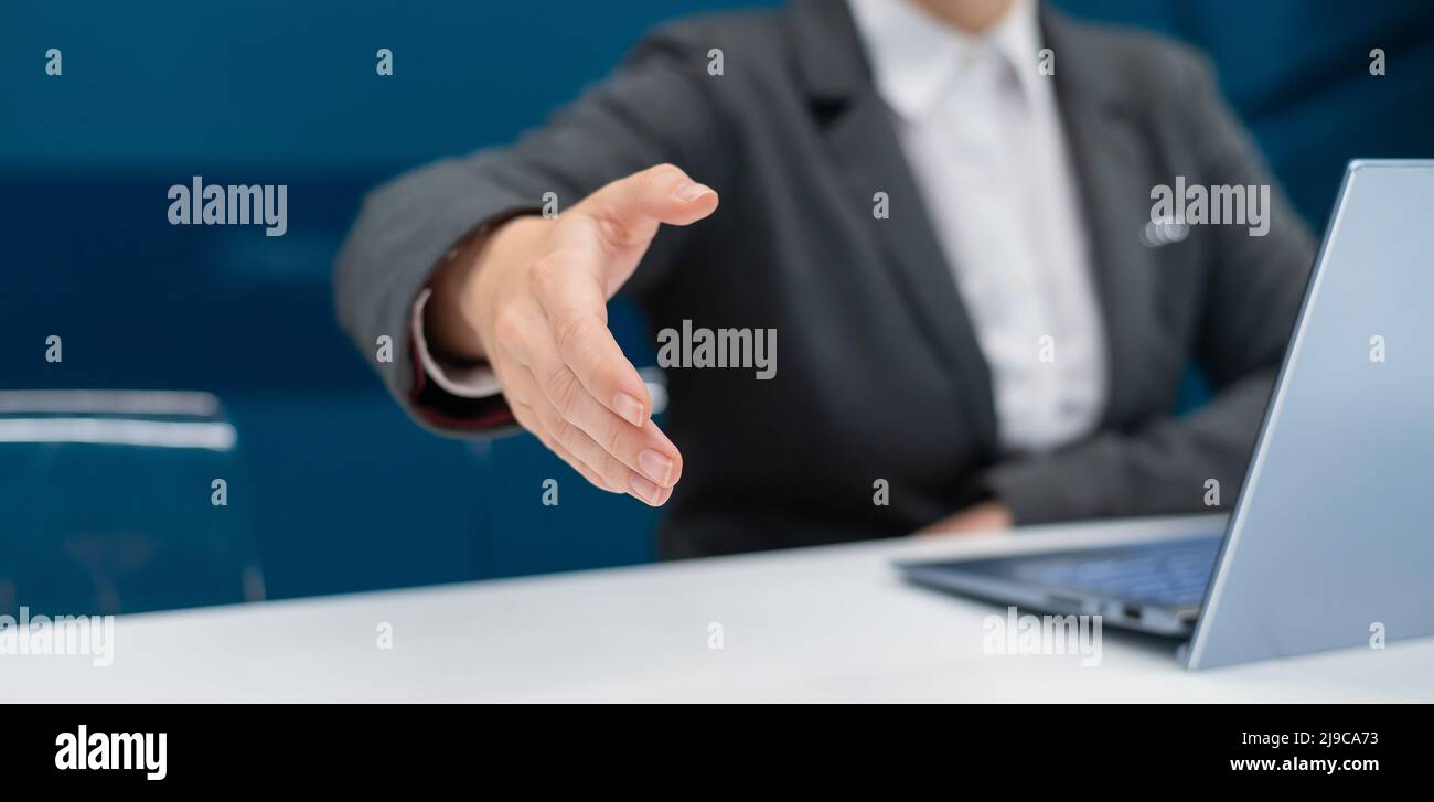 Gesichtslose Frau in einem Business-Anzug streut ihre Hand zum Händeschütteln, während sie an einem Schreibtisch sitzt. Weibliche Chefin macht einen erfolgreichen Deal. Stockfoto