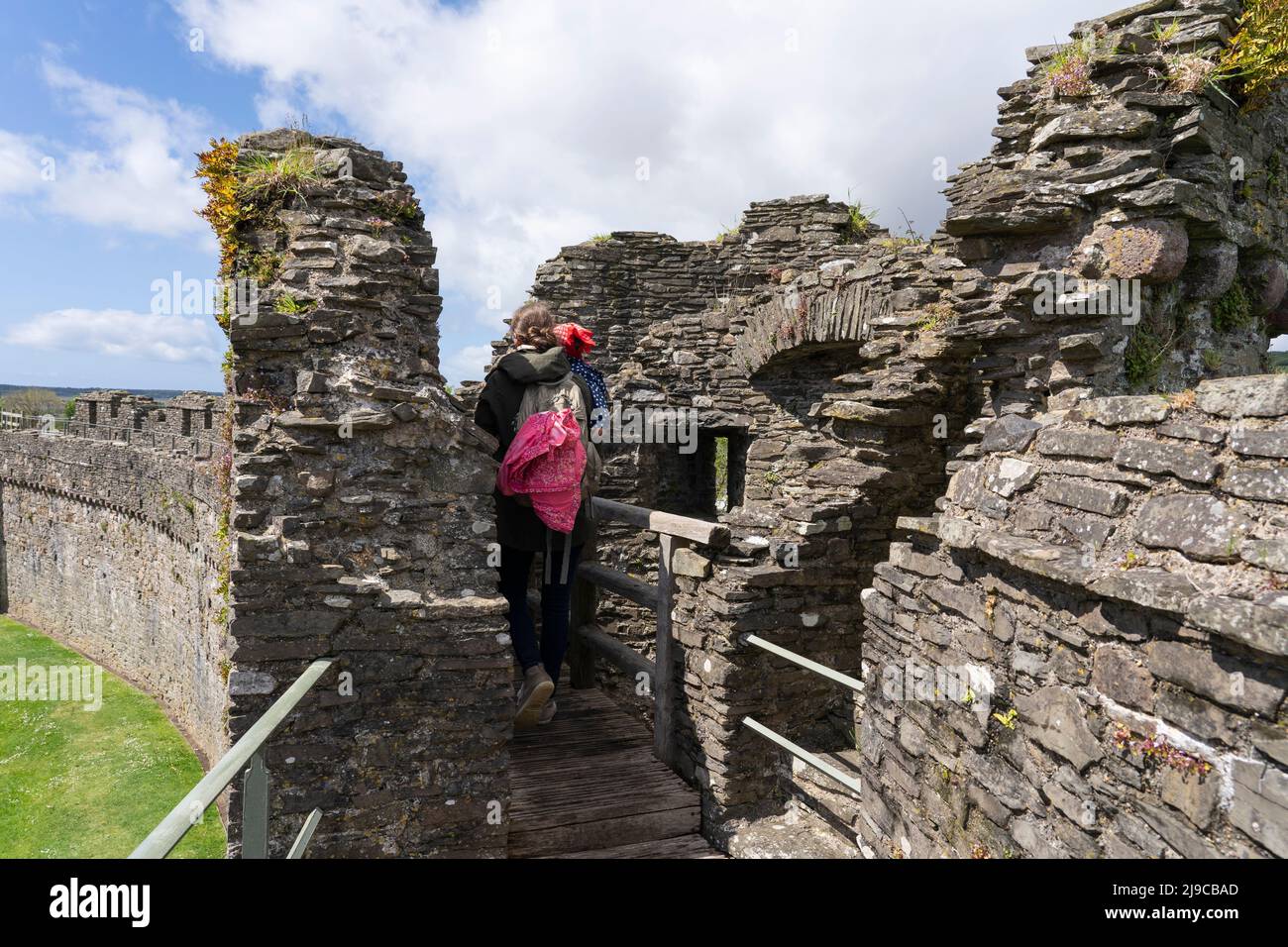 Eine Mutter und ihre junge Tochter, die auf den Zinnen der zerstörten Außenmauer von Kidwelly Castle, Kidwelly, Carmarthen, Wales, Großbritannien, wandern Stockfoto