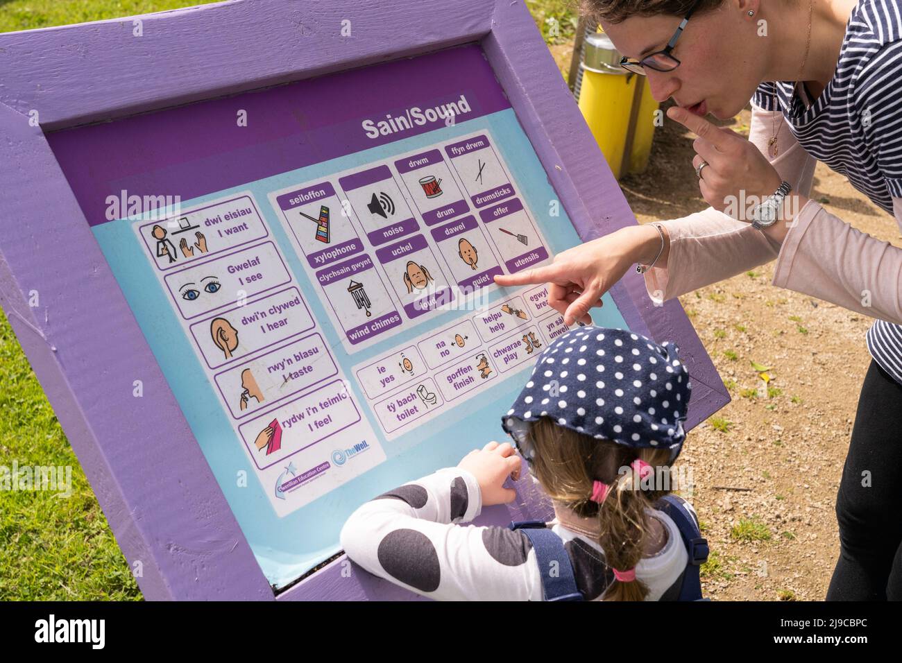 Eine Mutter, die ihrer Tochter auf einer walisisch-englischen Tontafel im Kindersensorik-Garten Kidwelly Wörter beibringt Stockfoto