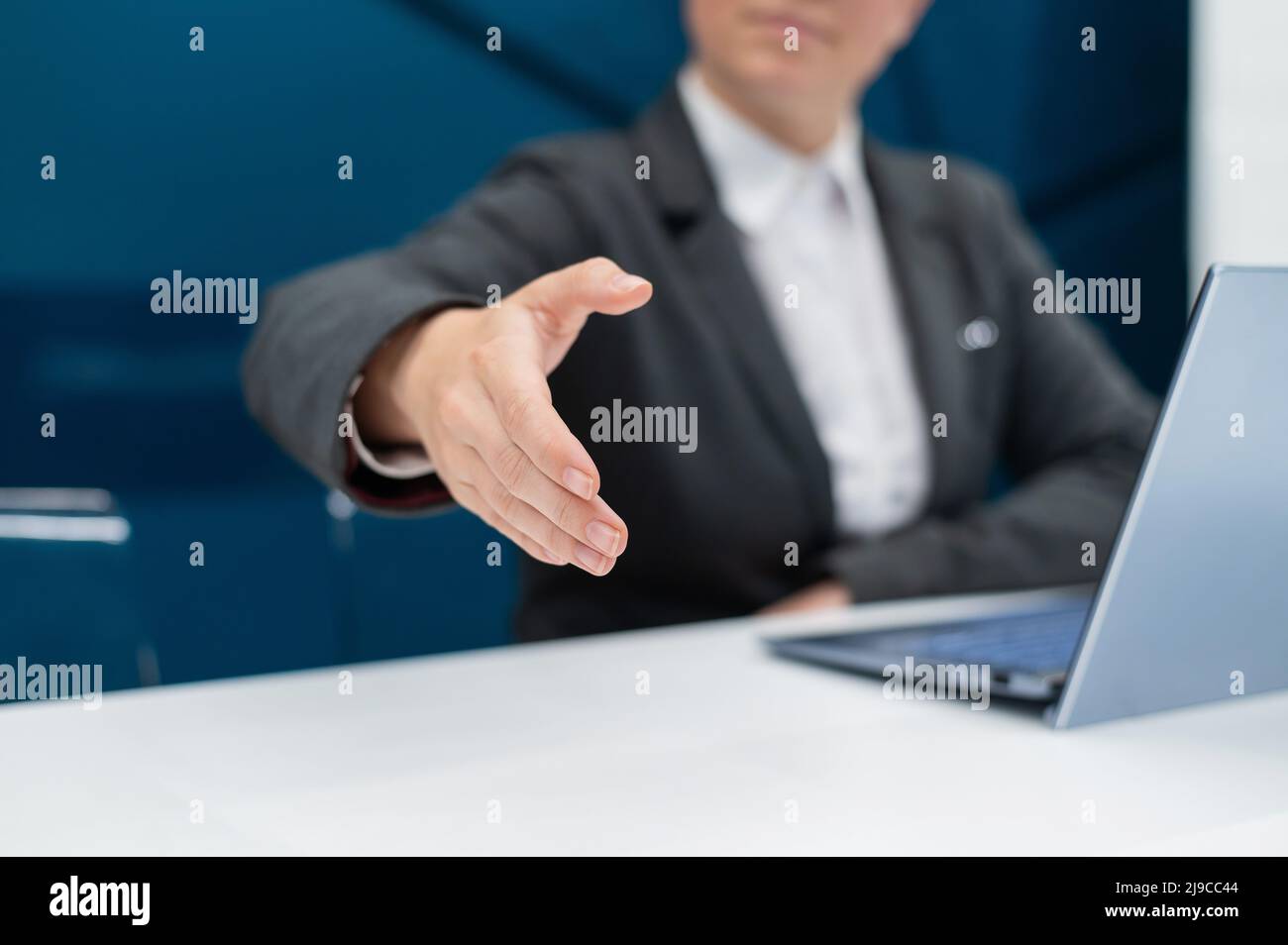 Gesichtslose Frau in einem Business-Anzug streut ihre Hand zum Händeschütteln, während sie an einem Schreibtisch sitzt. Weibliche Chefin macht einen erfolgreichen Deal. Stockfoto