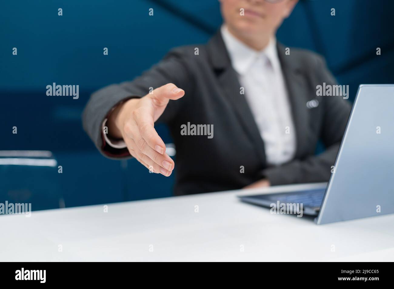 Gesichtslose Frau in einem Business-Anzug streut ihre Hand zum Händeschütteln, während sie an einem Schreibtisch sitzt. Weibliche Chefin macht einen erfolgreichen Deal. Stockfoto