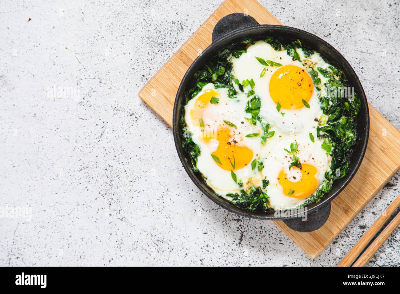 Grüne Shakshuka in einer gusseisernen Pfanne. Spiegeleier mit Spinat und gebratenem Toast. Gesundes, nahrhaftes Frühstück, Stockfoto