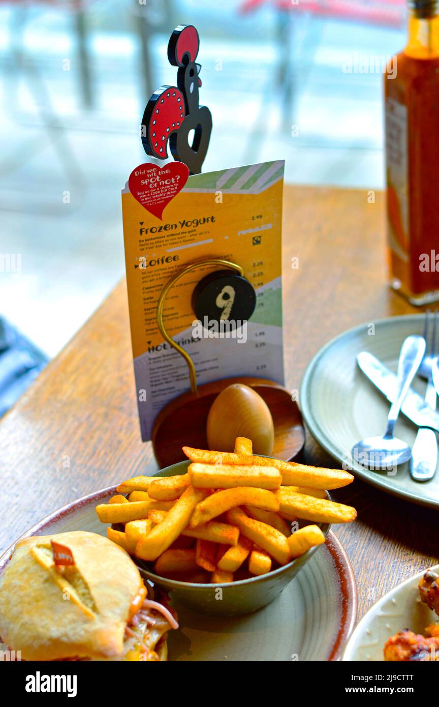 16. Juni 2016. Ein Nando's Restaurant in Großbritannien. Ein Esstisch im Restaurant von Nando mit Menü, Logo, Burger, Pommes Frites und Sauce. Stockfoto