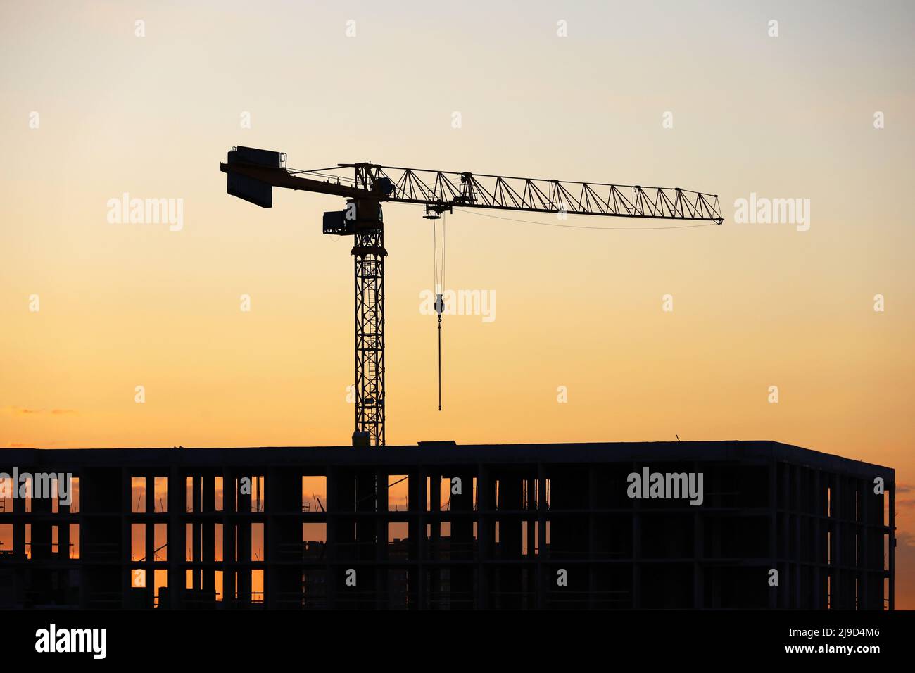 Silhouette eines Turmdrehkrans über dem unfertigen Gebäude bei Sonnenaufgang. Wohnungsbau, Wohnblock in der Stadt auf dem Hintergrund Stockfoto