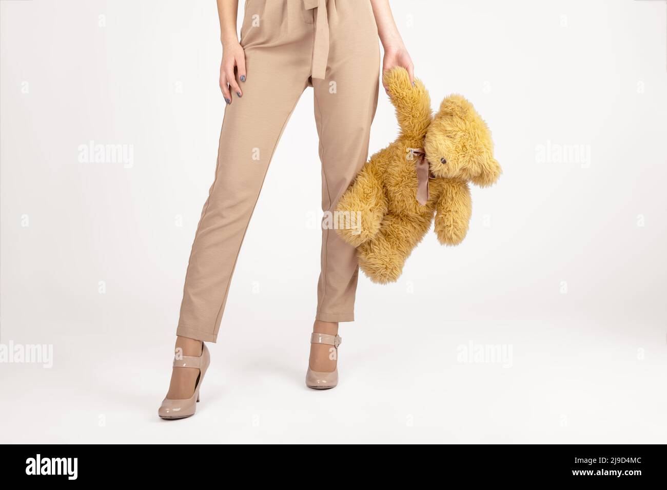 Frau und Kind, Modekonzept. Schlanke und schöne Frau mit beigefarbener Hose und T-Shirt ohne Ärmel, die flauschiges, braunes Bärenspielzeug in den Händen hält. Stockfoto