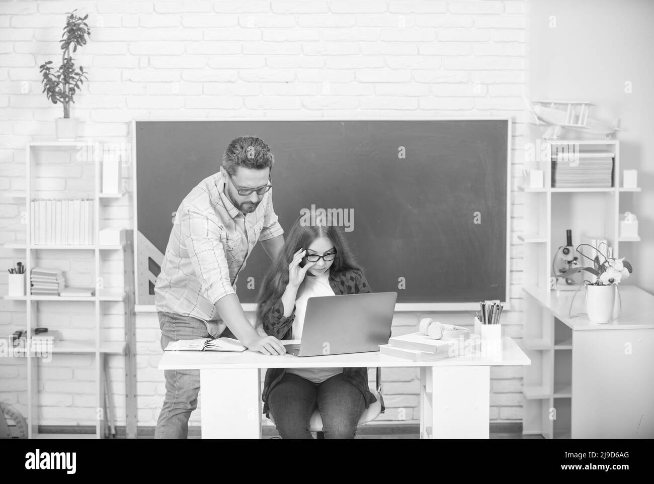 Neugieriger Vater und Kind studieren in der Schule mit Laptop auf Tafel Hintergrund, zurück zur Schule Stockfoto