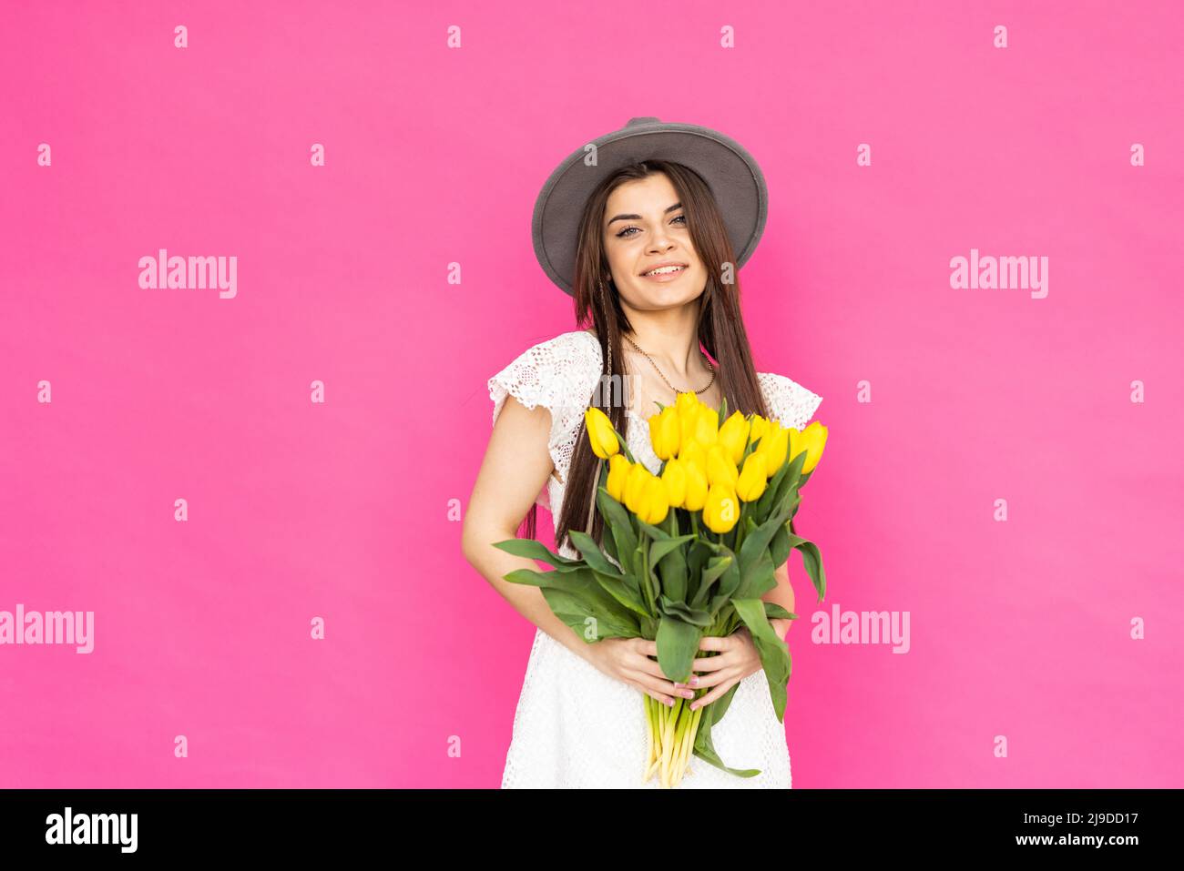 Frühlingsblumen. Junge wunderschöne Mädchen in einem leuchtend rosa Kleid schaut in der Kamera mit einem großen Lächeln, hält ein paar Tulpen in den Händen. Stockfoto