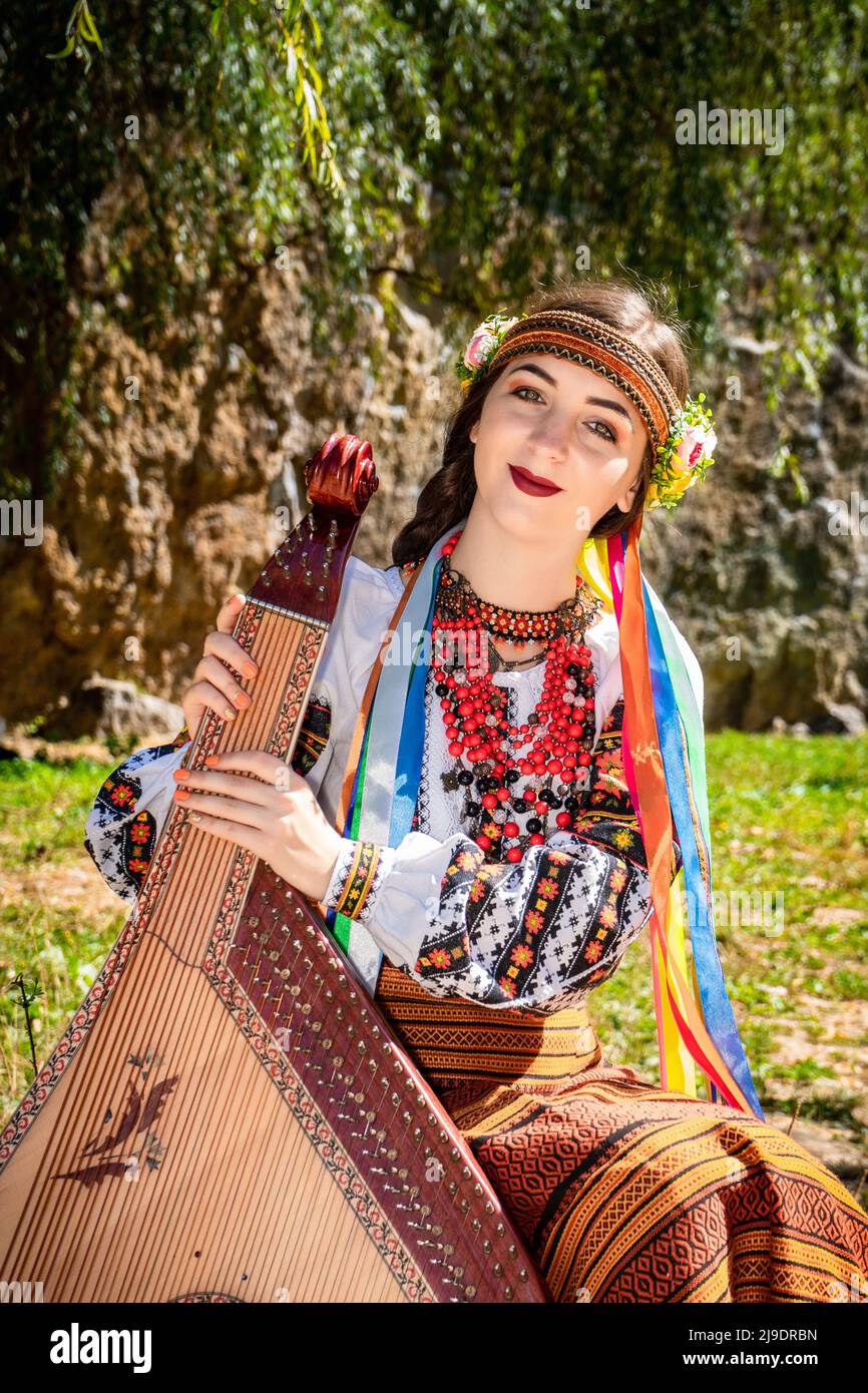 Ukrainischer Musiker in authentischer Nationaltracht sitzt an einem Felsen. Ukrainische Frau mit einem Bandura-Musikinstrument, bevor sie Volksmusik aufführt Stockfoto