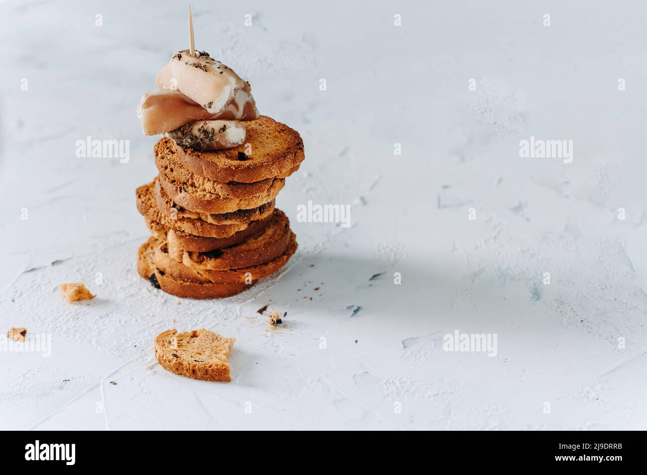 Hintergrund der Speisen. Ein Turm aus knusprigen Toast mit Oliven und Schinken- und Frischkäse-Häppchen auf einem texturierten, eleganten weißen Hintergrund. Knuspriger Toast für mehr Farbe Stockfoto