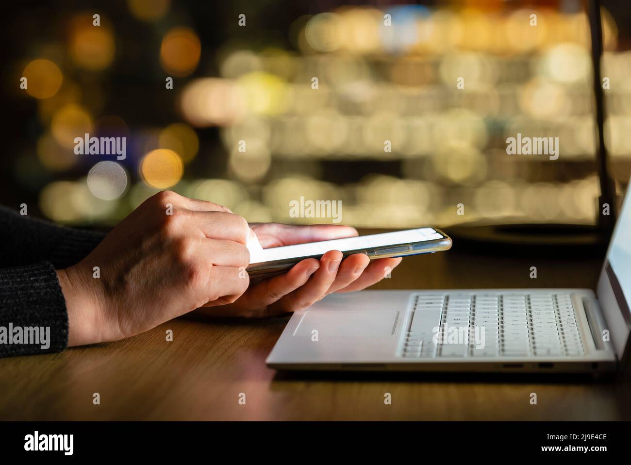 Mit Smartphone und Laptop bei Nacht, ohne Fokus City Skyline Hintergrund Stockfoto