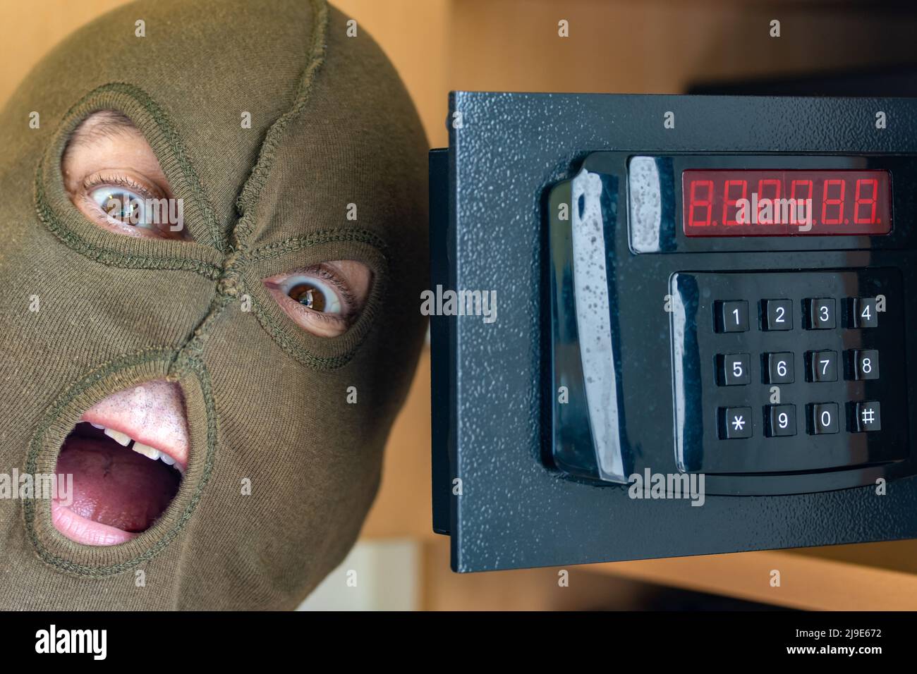 Ein fröhlicher Mann in einer Maske feiert den Erfolg, indem er einen Safe auf einem numerischen Code öffnet Stockfoto
