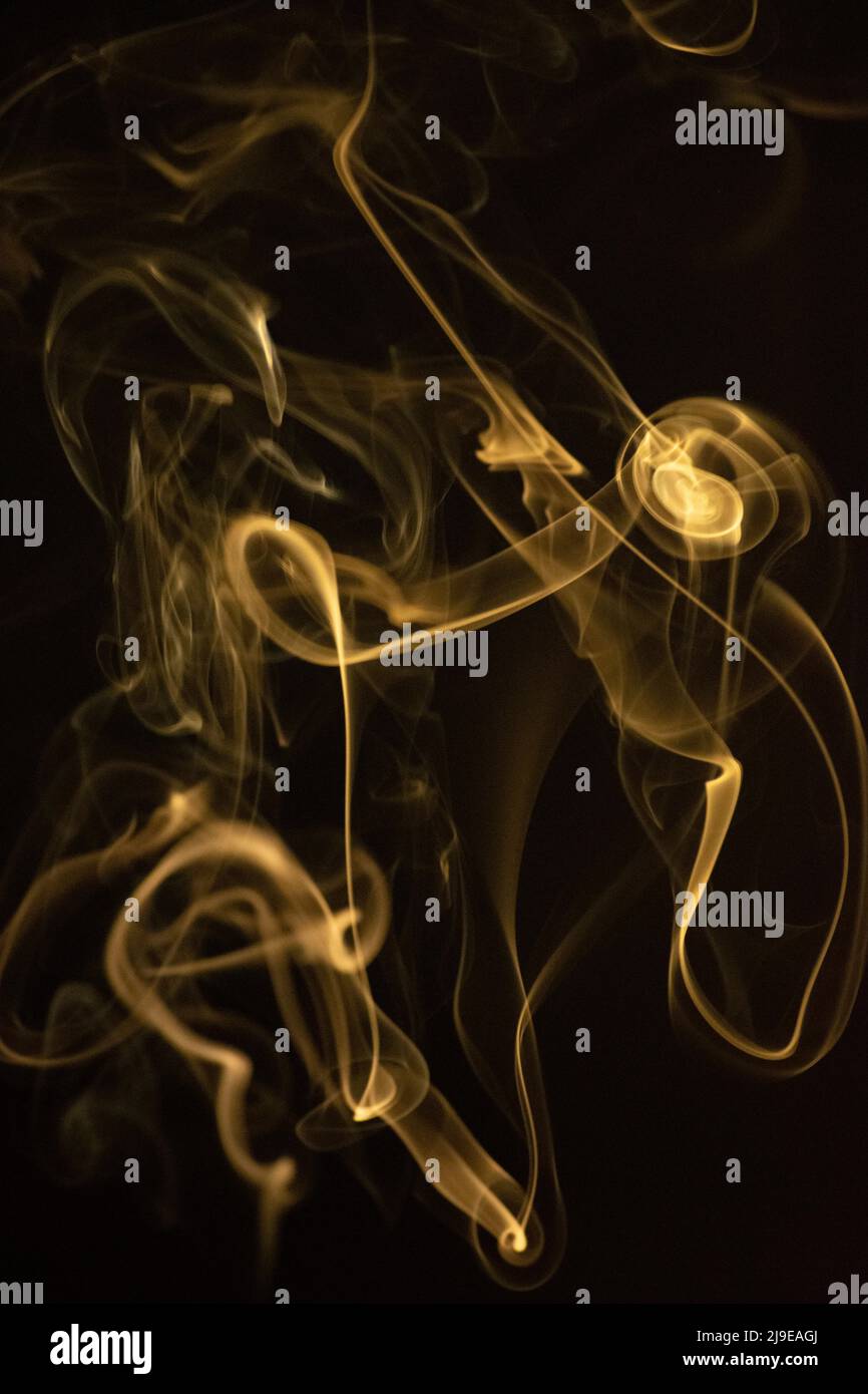 Ein wirbelndes, aufsteigendes Rauchmuster mit einer gelblich-goldenen Farbe auf schwarzem Hintergrund, Foto könnte als Hintergrund, Rauchstruktur oder abstrakt verwendet werden, Stockfoto