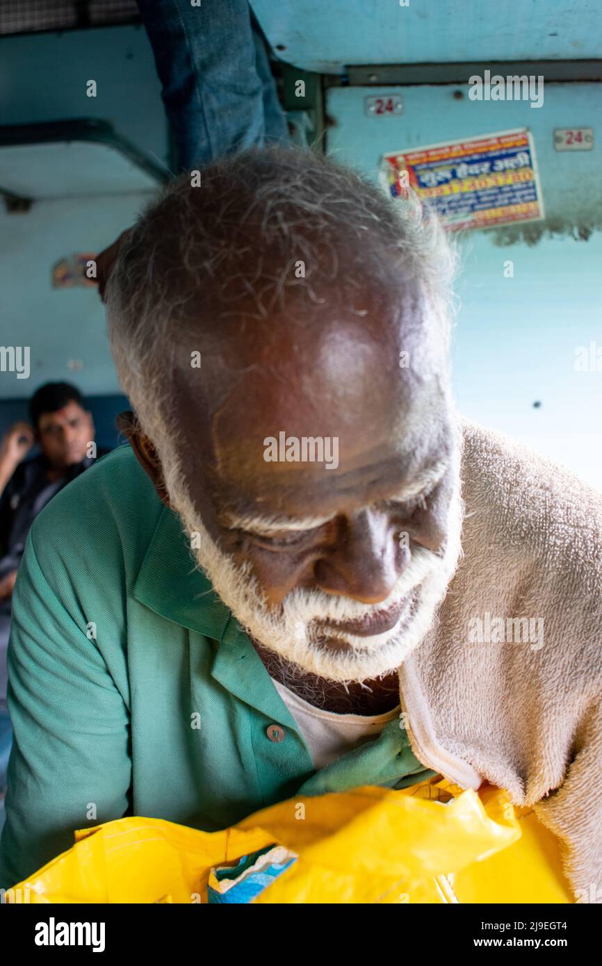 Unbefangenes Porträt eines älteren indischen Mannes mit weißem Haar und Bart, der sich über Gepäck in einem Passagierwagen eines Zuges in Indien lehnt Stockfoto