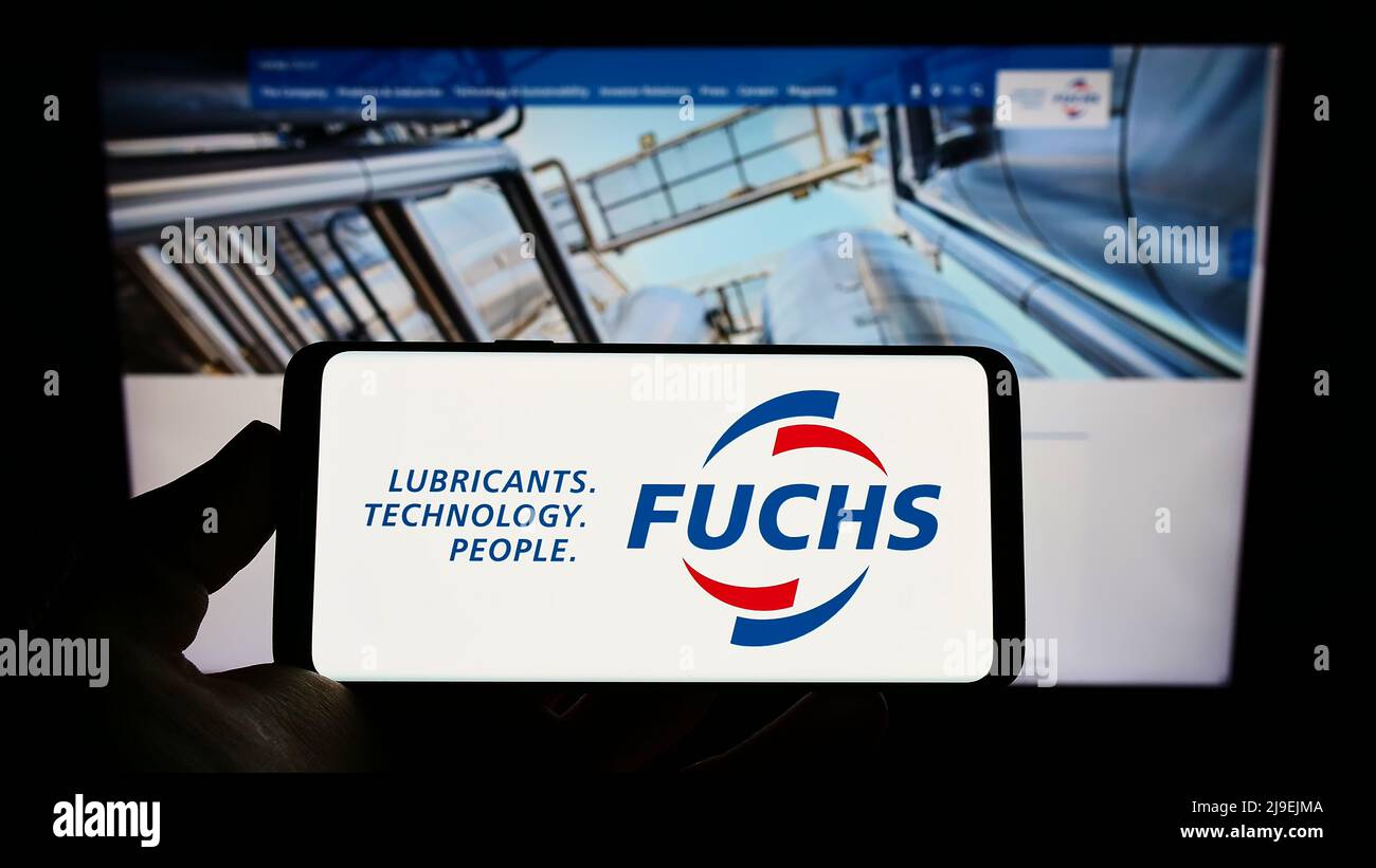 Person, die Mobiltelefon mit Logo des deutschen Schmierstoffunternehmens Fuchs Petrolub SE auf dem Bildschirm vor der Business-Webseite hält. Konzentrieren Sie sich auf die Telefonanzeige. Stockfoto