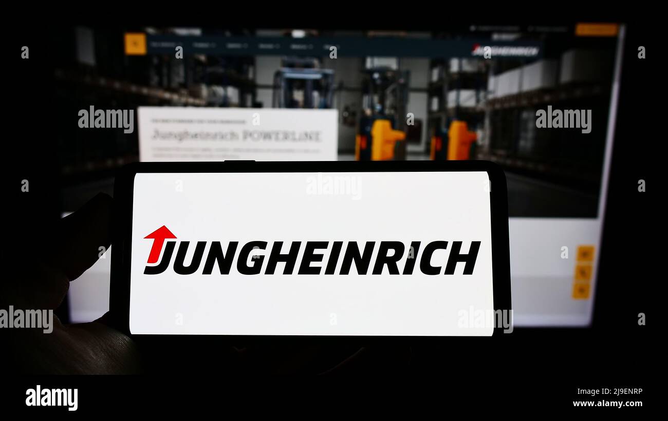 Person, die Mobiltelefon mit Logo des deutschen Ingenieurunternehmens Jungheinrich AG auf dem Bildschirm vor der Business-Webseite hält. Konzentrieren Sie sich auf die Telefonanzeige. Stockfoto