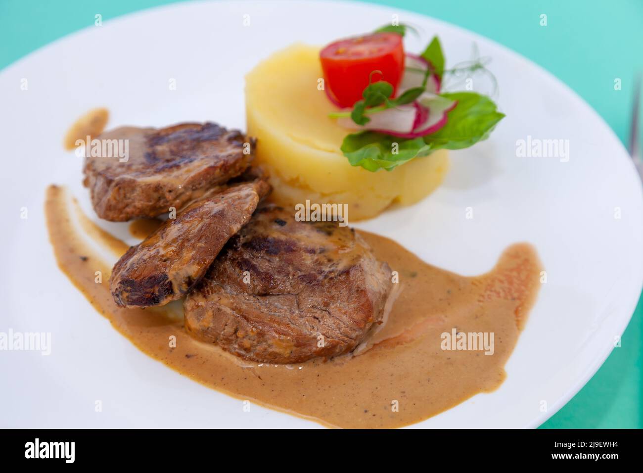 Fleischbällchen mit Kartoffelpüree auf einem weißen Teller. Fleisch in saurer Rahmsoße. Tomaten und Basilikum. Essen im Restaurant. Mittagspause. Medaillons. Stockfoto