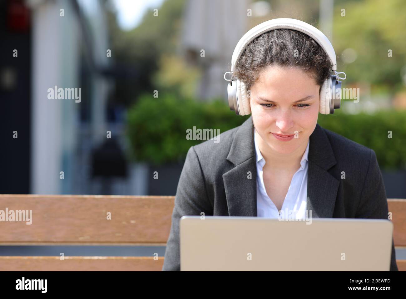 Geschäftsfrau mit kabellosen Kopfhörern und Laptop auf der Bank Stockfoto