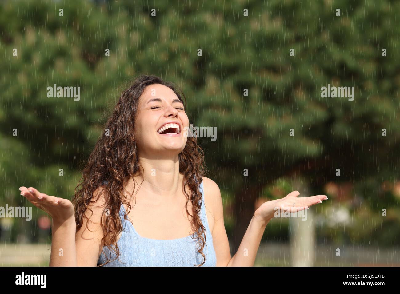 Glückliche Frau, die lachend und unter plötzlichem Regen an einem sonnigen Tag genießt Stockfoto