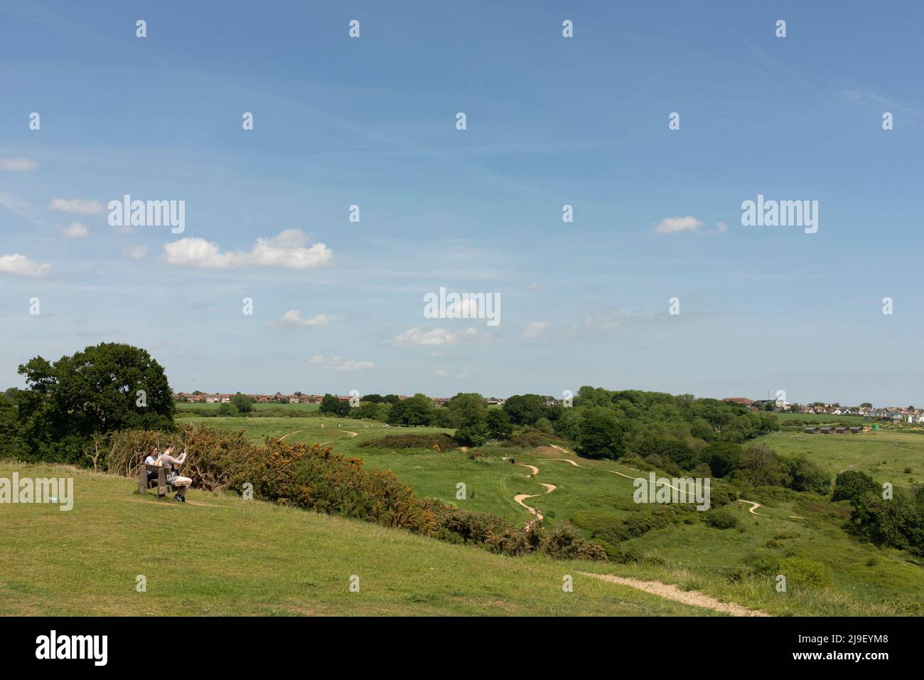 Zwei junge Menschen sitzen auf einer Bank im Hadleigh Country Park, Essex, England, mit Radwegen im Hintergrund (ein Vermächtnis der Olympischen Spiele 2012) Stockfoto