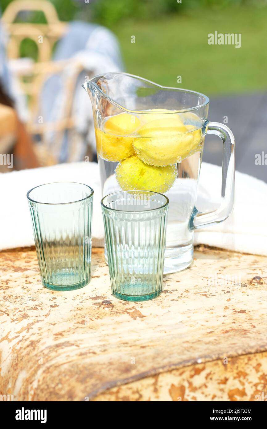 Wasserkrug mit Wasser und Zitronen mit zwei Gläsern im Garten Stockfoto