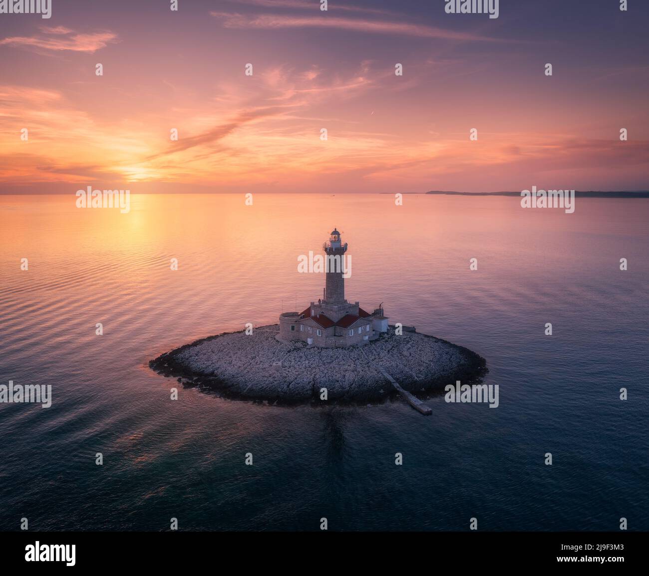 Leuchtturm auf einer kleinen Insel im Meer bei farbenfrohem Sonnenuntergang im Sommer Stockfoto