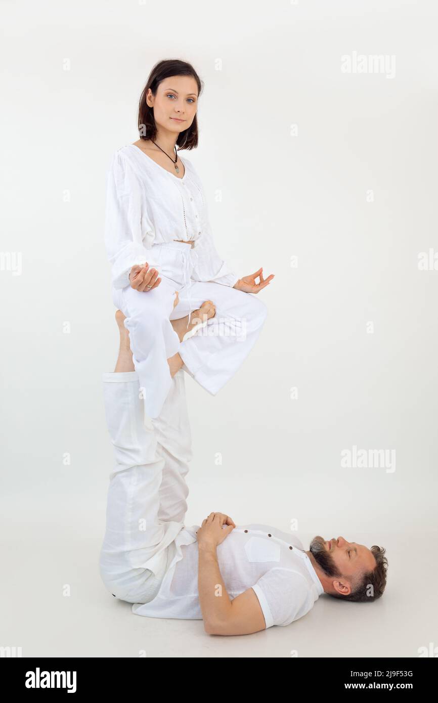Vertikale Männer und Frauen machen Yoga-Akrobatik. Männchen, auf dem Boden liegend, an den Beinen weiblich halten, auf den Füßen sitzen. Skoliose-Behandlung Stockfoto