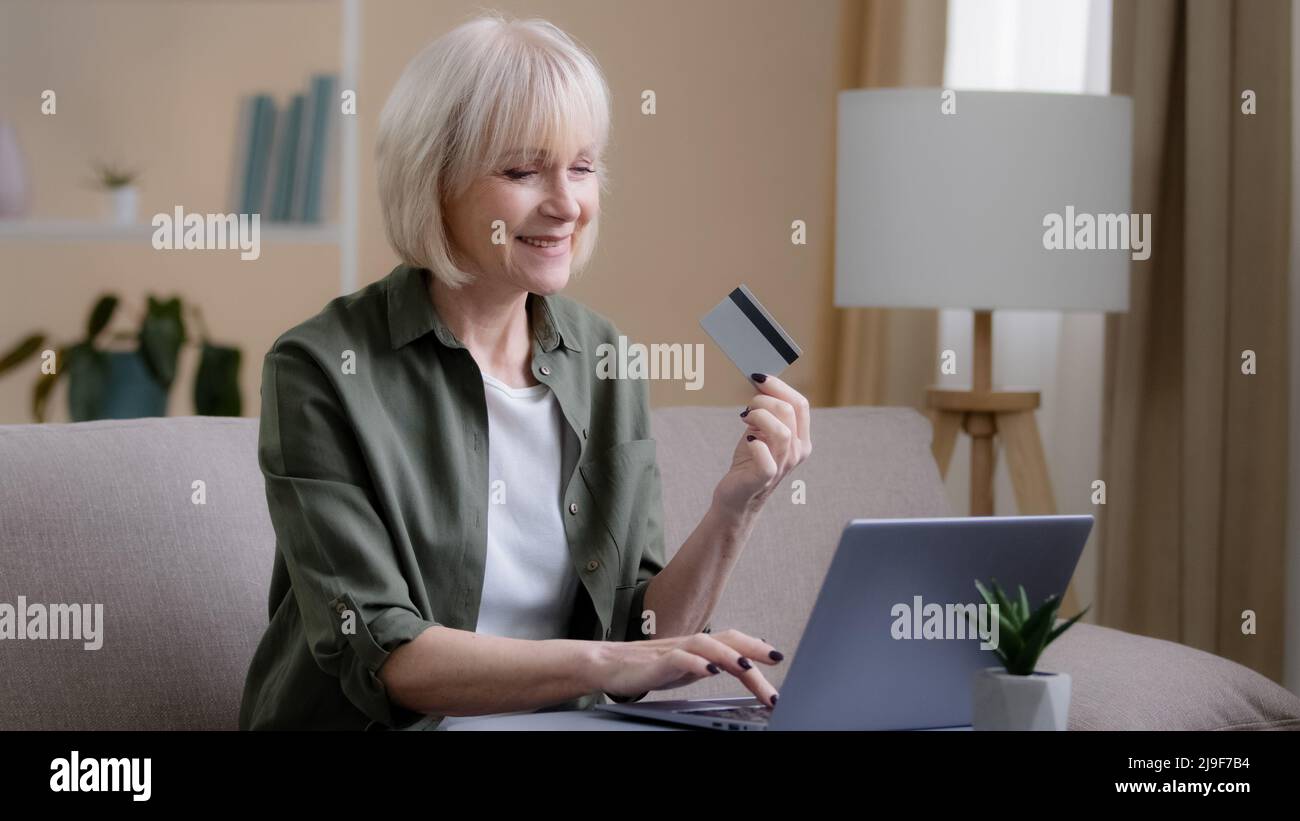 Ältere kaukasische 60s Frau Internet-Shopping auf Laptop zu Hause. Ältere Erwachsene reife Dame E-Commerce-Kauf Zahlung in Computer-App virtuelles Geld mit Stockfoto