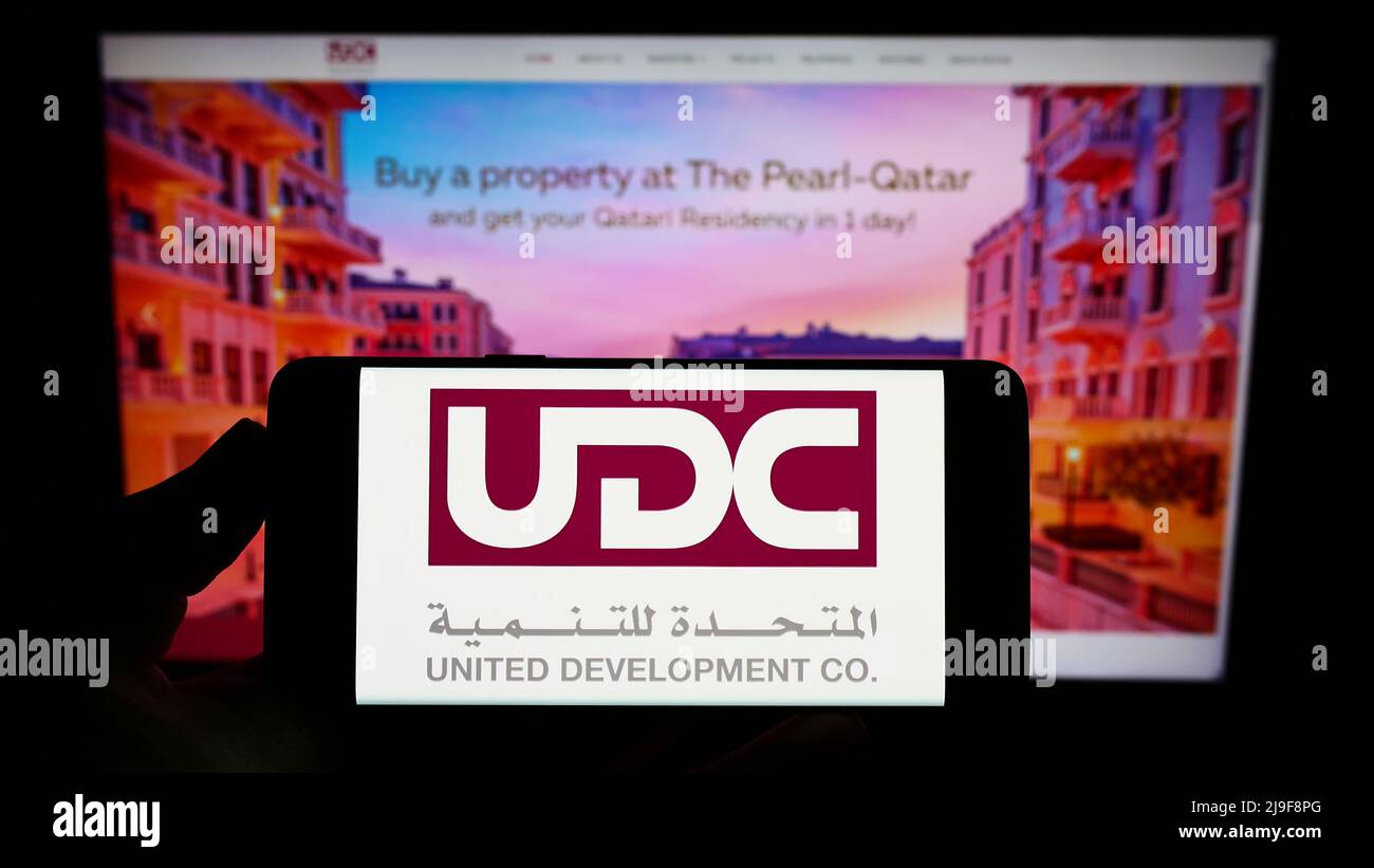 Person mit Smartphone und Logo der United Development Company Q.P.S.C. (UDC) auf dem Bildschirm vor der Website. Konzentrieren Sie sich auf die Telefonanzeige. Stockfoto