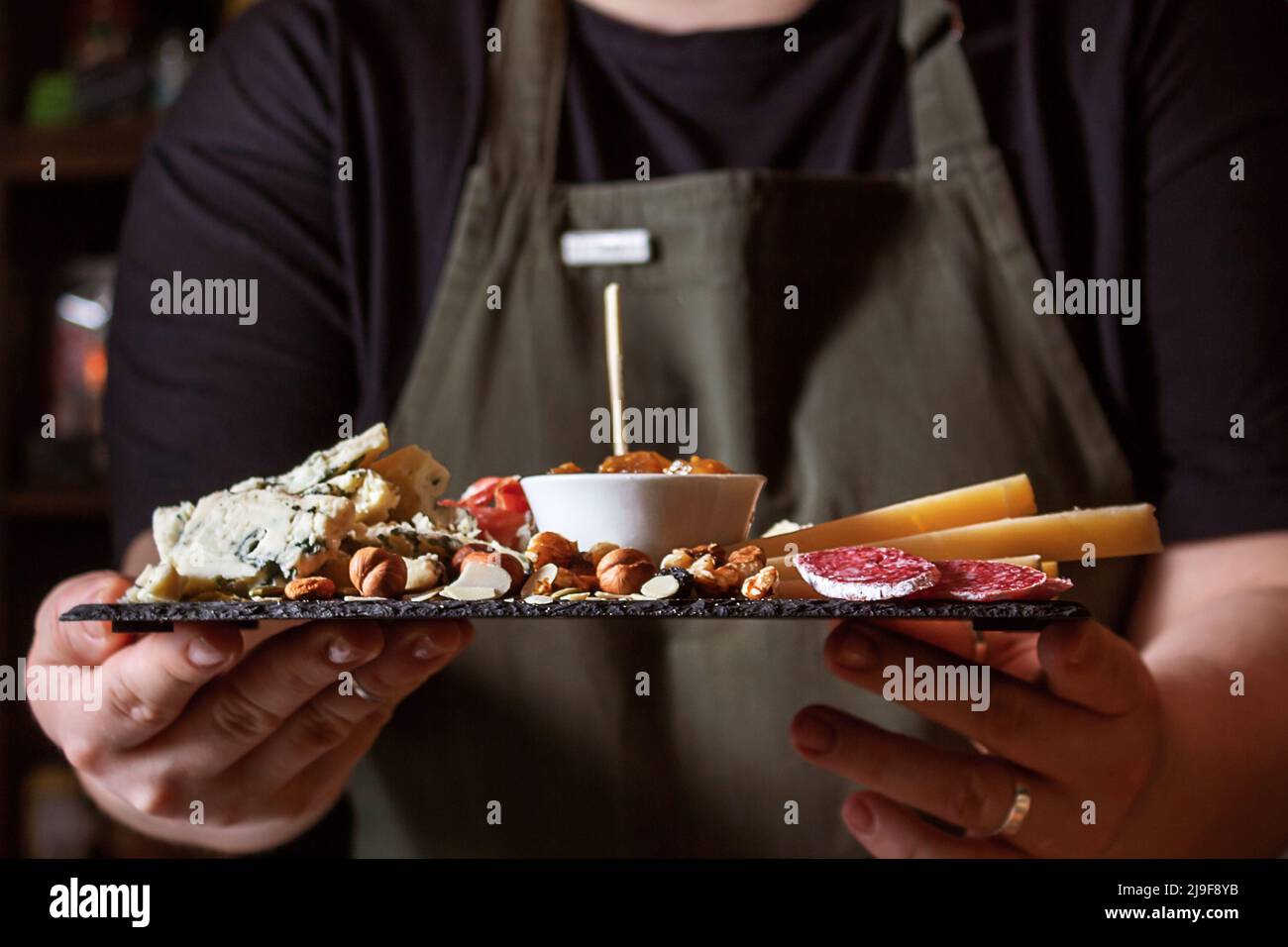 Kellnerin hält schwarzes Steinbrett mit Delikatessen. Stockfoto