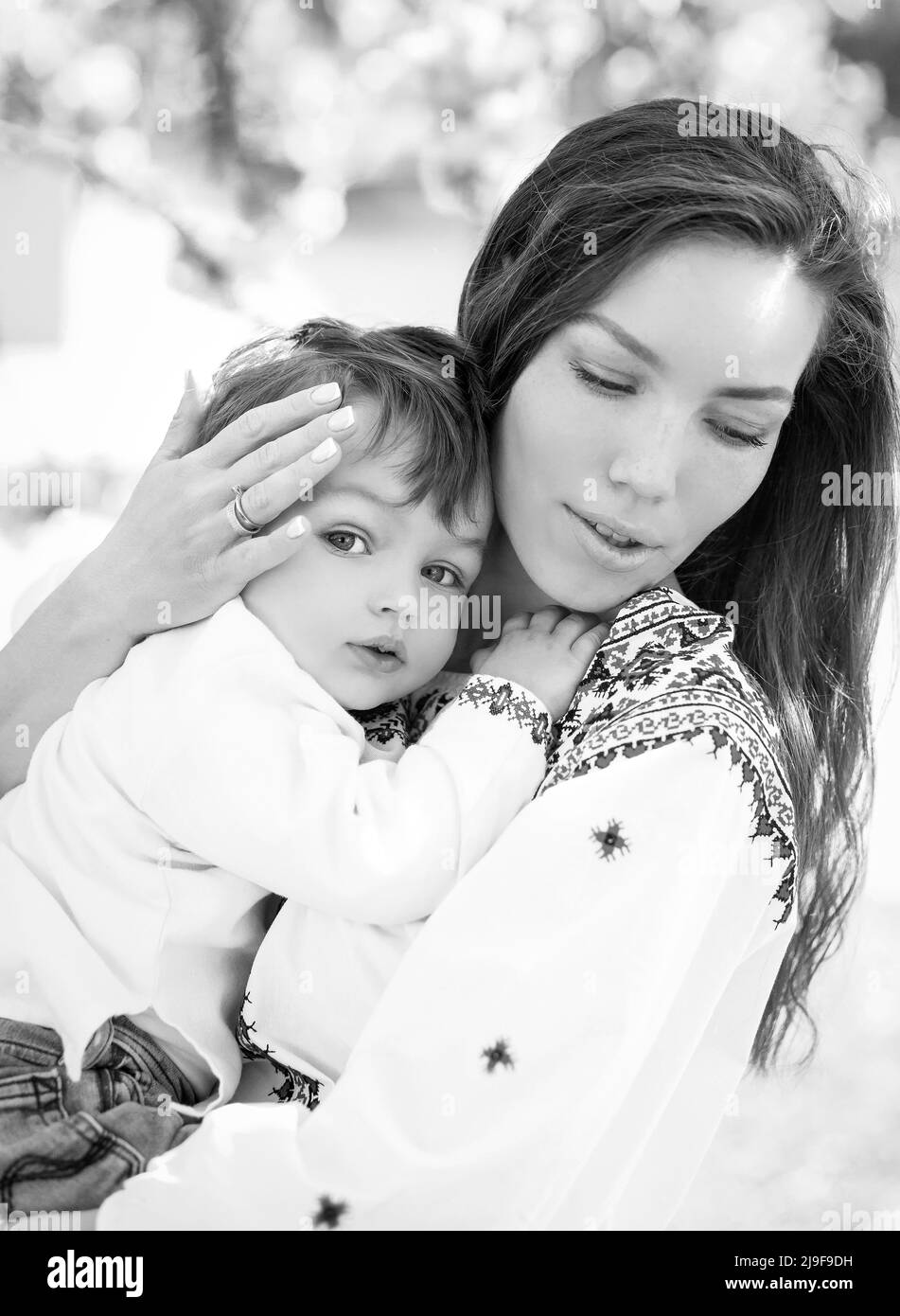 Schwarz-Weiß-Foto kleines Baby auf den Händen der Mutter. Porträt einer Familie von zwei Personen. Frühling Landschaft Hintergrund. Stockfoto